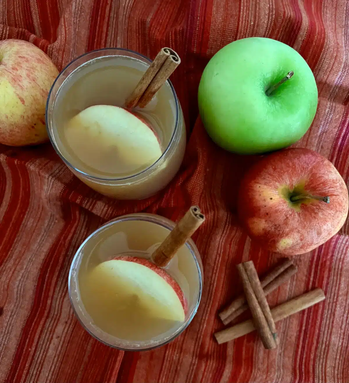 overhead photo of two glasses of homemade apple cider with apples and cinnamon sticks